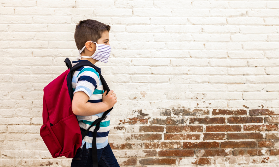 Kid in a mask walking with a backpack