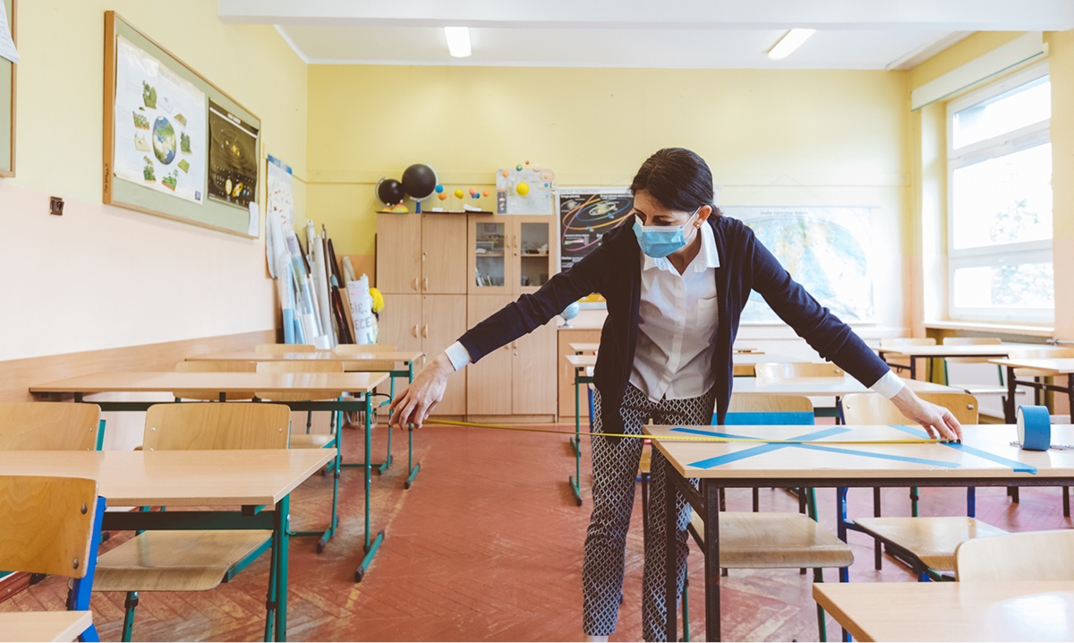 A teacher in a mask measures between desks