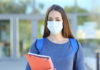 A teenager wearing a mask and holding a notebook