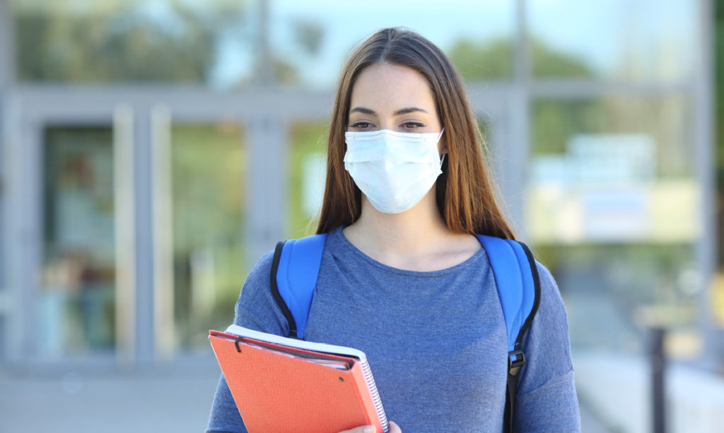 A teenager wearing a mask and holding a notebook