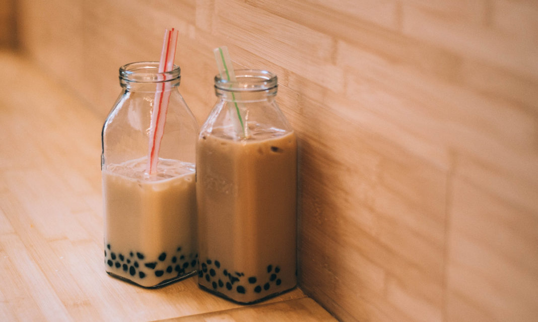 Teo containers of bubble tea next to a wood wall