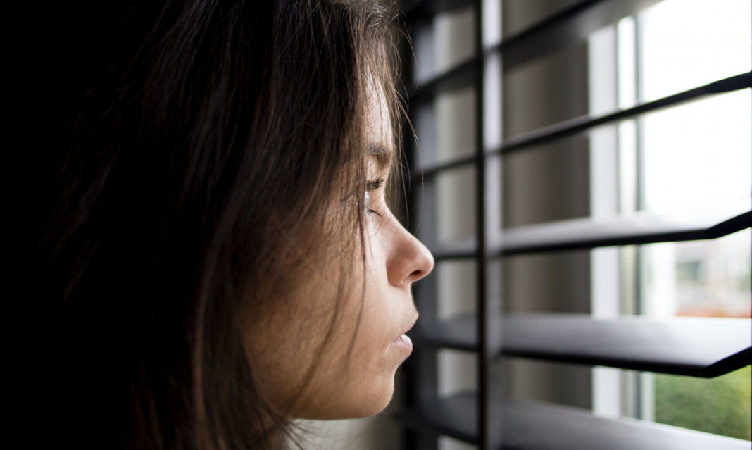 A young girl looking out closed blinds