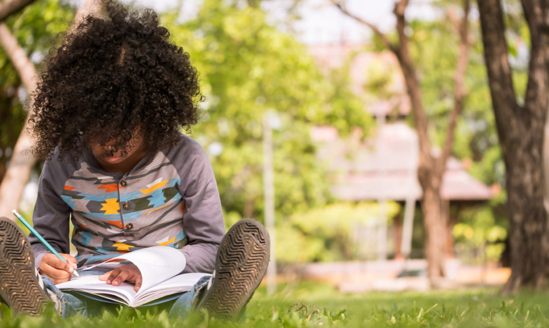 Child outside writing in a book