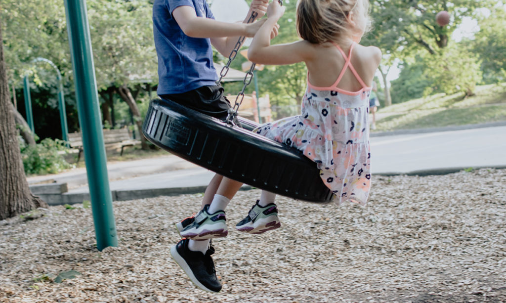 Two kids playing on a tire swing