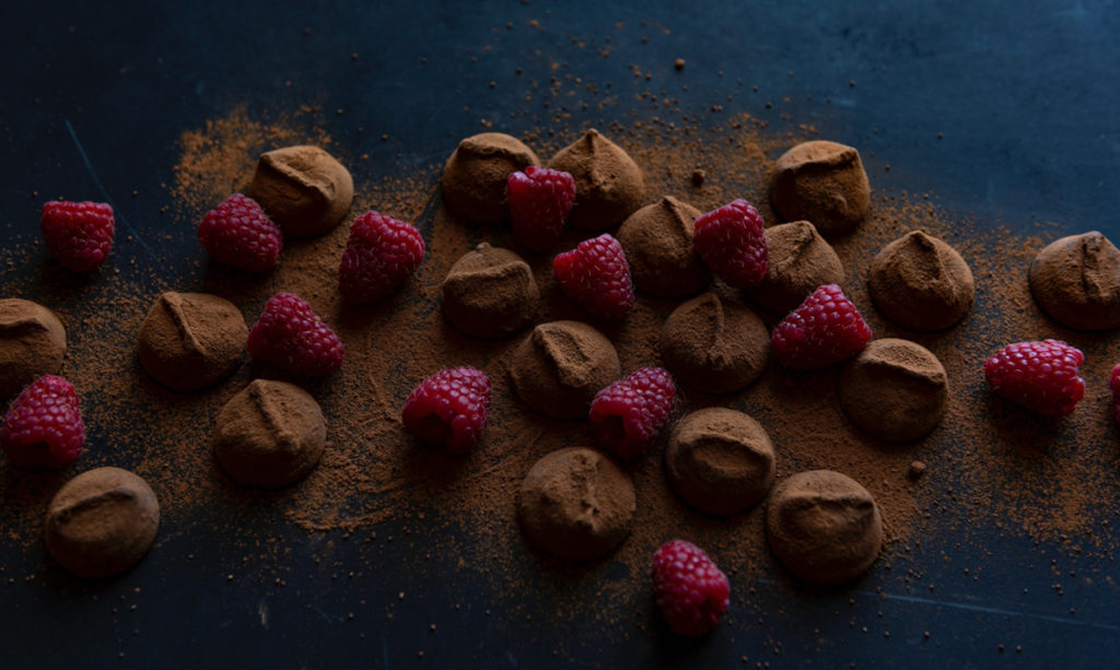 Bonbons covered in chocolate powder and surrounded by raspberries