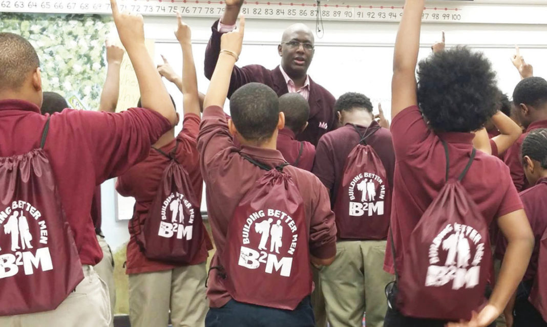 Group of young boys from Building Better Men raise their hands while looking at Odis Bellinger