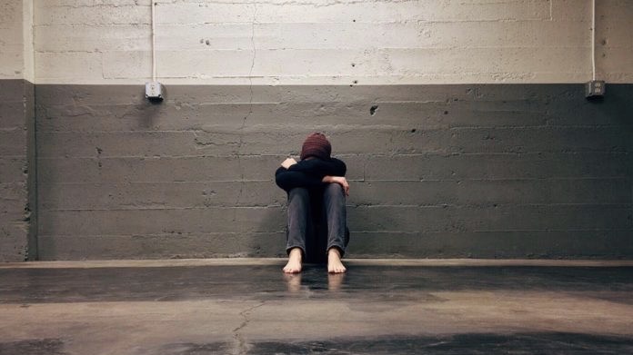 Barefoot teen sitting up against a wall with their head in their arms