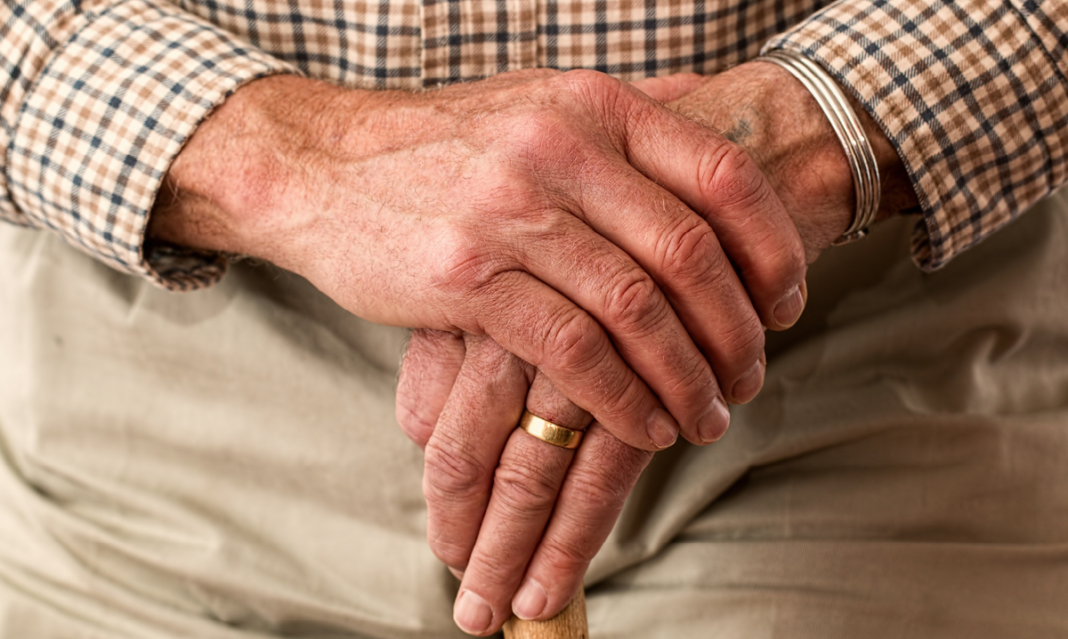 A pair of old hands folded on a cane