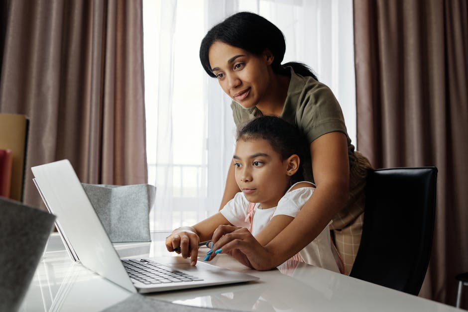 Woman helping a young girl on a laptop