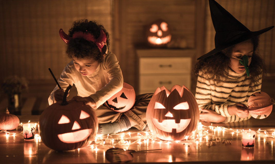 Two girls in costume carving pumpkins