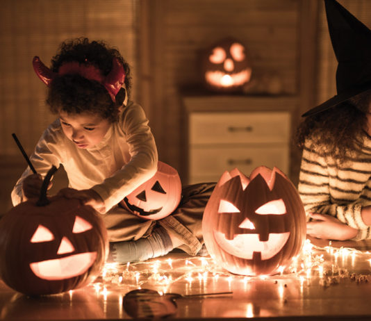 Two girls in costume carving pumpkins