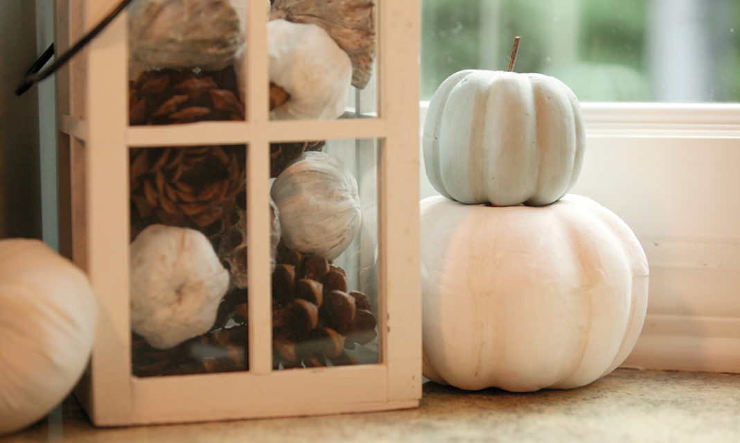 White pumpkins stacked next to a lantern filled with fake pumpkins and pinecones