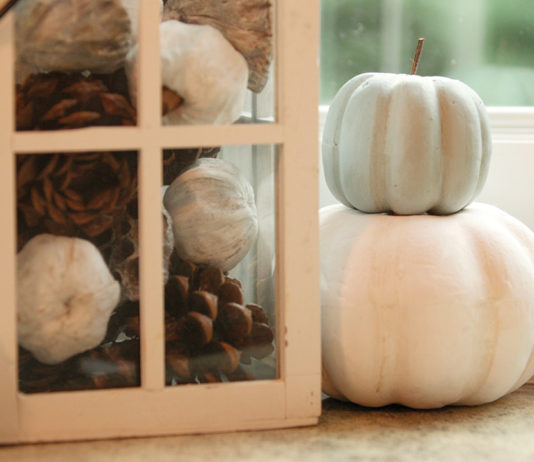 Halloween 2020 Celebration Ideas for Families White pumpkins stacked next to a lantern filled with fake pumpkins and pinecones