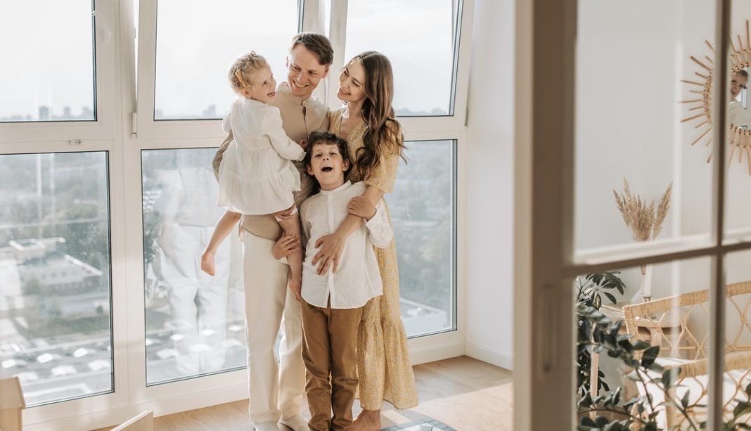 Family of four laughing with each other in front of a window