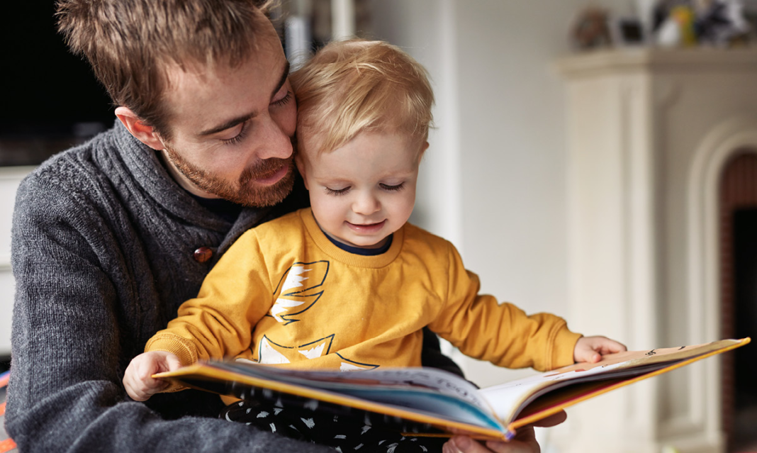 a man holding a baby who is holding an open book