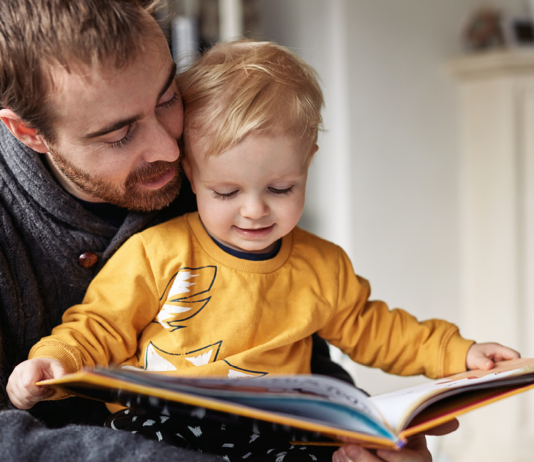 a man holding a baby who is holding an open book
