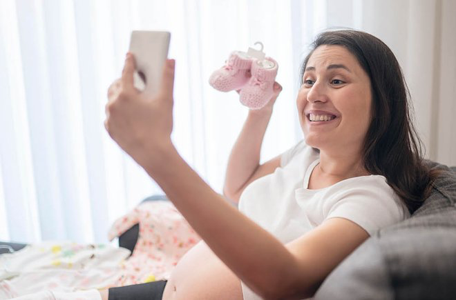 Woman holding up a pair of pink baby booties while on her phone