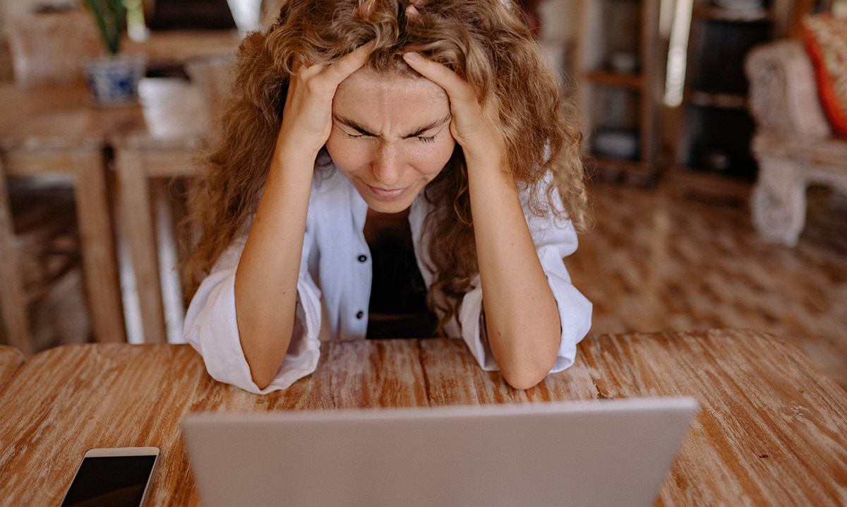 Woman crying with her head in her hands while looking at a laptop