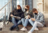 Three college-aged kids sitting on steps while wearing face masks