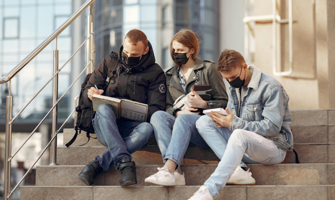 Three college-aged kids sitting on steps while wearing face masks