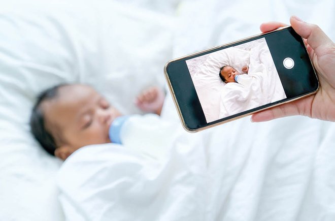 A hand holding a smart phone over a sleeping baby