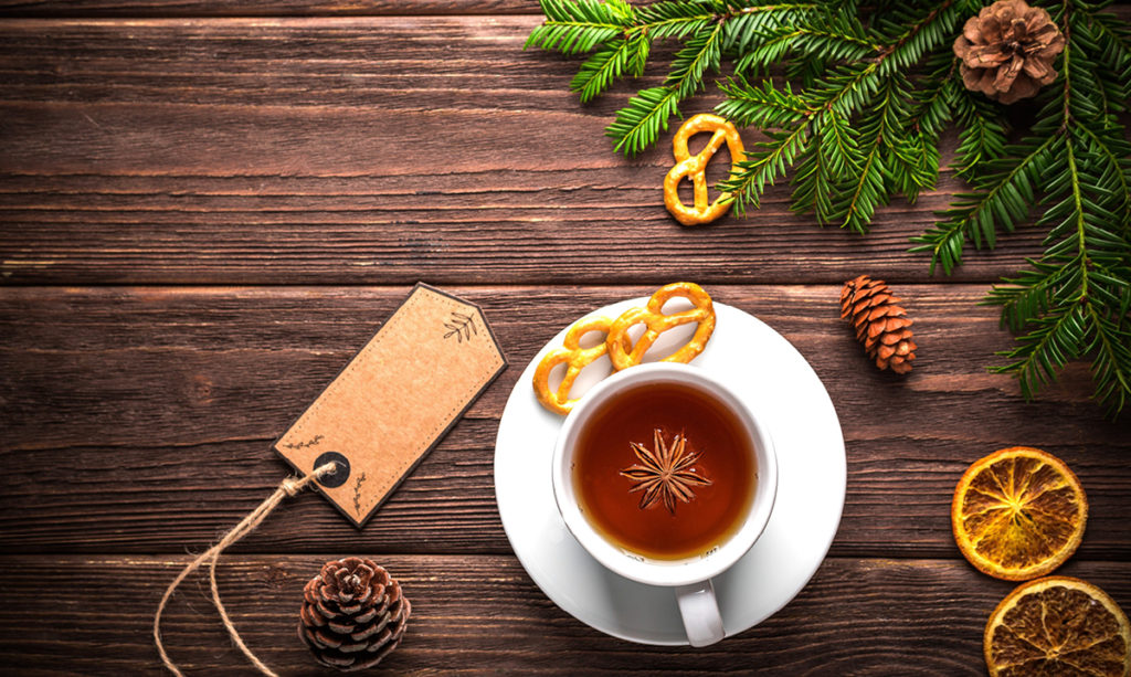 Cup of tea surrounding by winter greenery on a wooden plank table