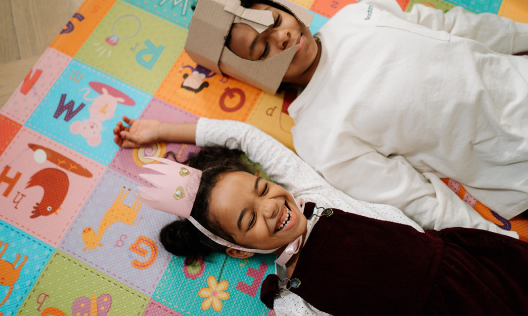 Two young Black kids smiling while wearing costumes and laying on the floor