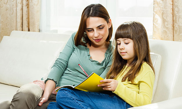 Woman and girl sitting on couch looking at piece of paper