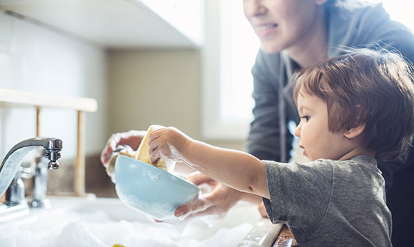 A parent helps their child wash the dishes