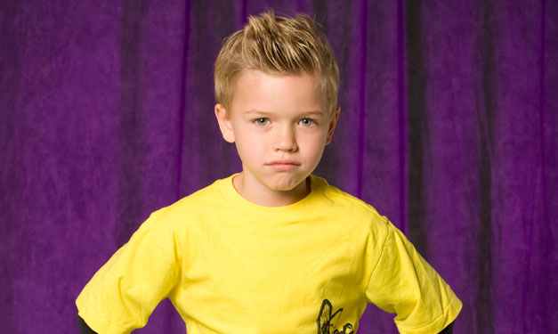 Boy with hands on his hips in front of a purple curtain