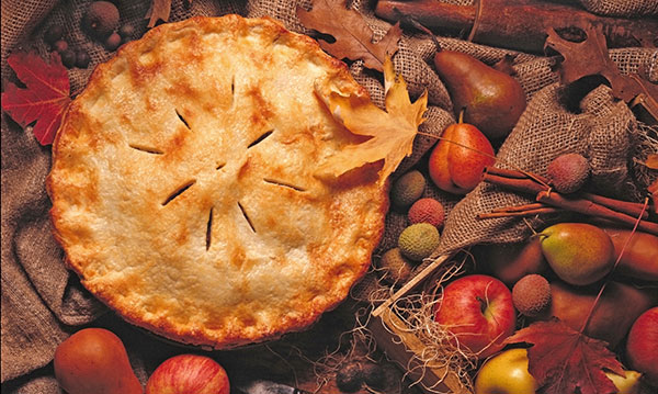 A full apple pie surrounded by apples and leaves on a wood table