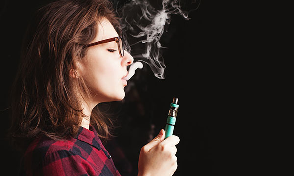 Teen girl exhales after taking a puff from a vape