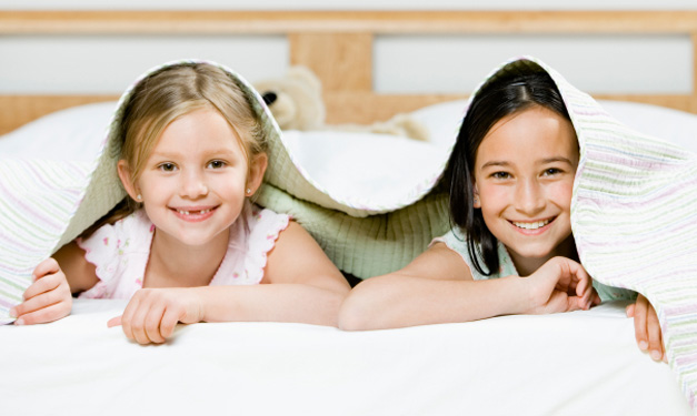 Two girls smiling from under a blanket