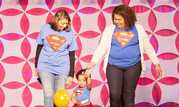 Two women and a little girl in Superman shirts walk the runway