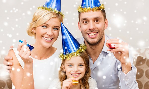 Woman, man and child in blue and gold party hats with noisemakers surrounded by white orbs