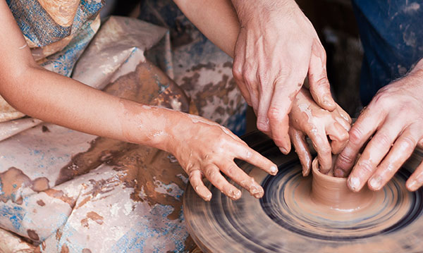 Child hands and adult hands making a pot on a pottery wheel