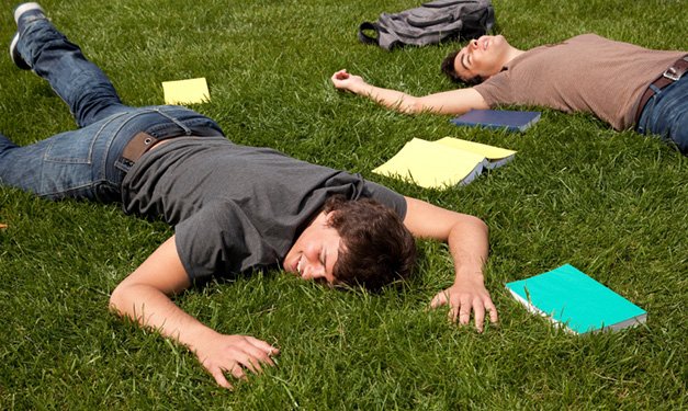 Two high school boys laying on grass surrounded by notebooks