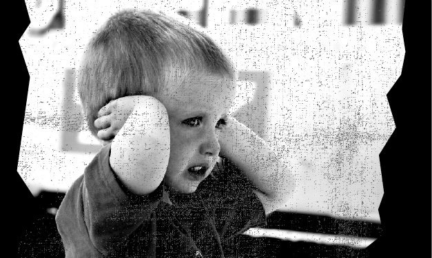 Young boy holds his ears while looking pained