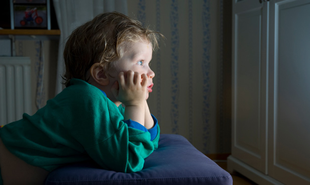 A young child in a green sweater glued to the TV screen
