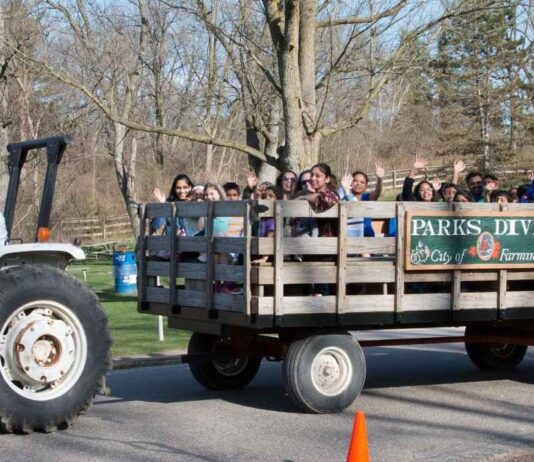 Families enjoy a hayride at Heritage Park during Hay Day in Farmington Hills with kids and parents waving while riding a tractor-pulled wagon.