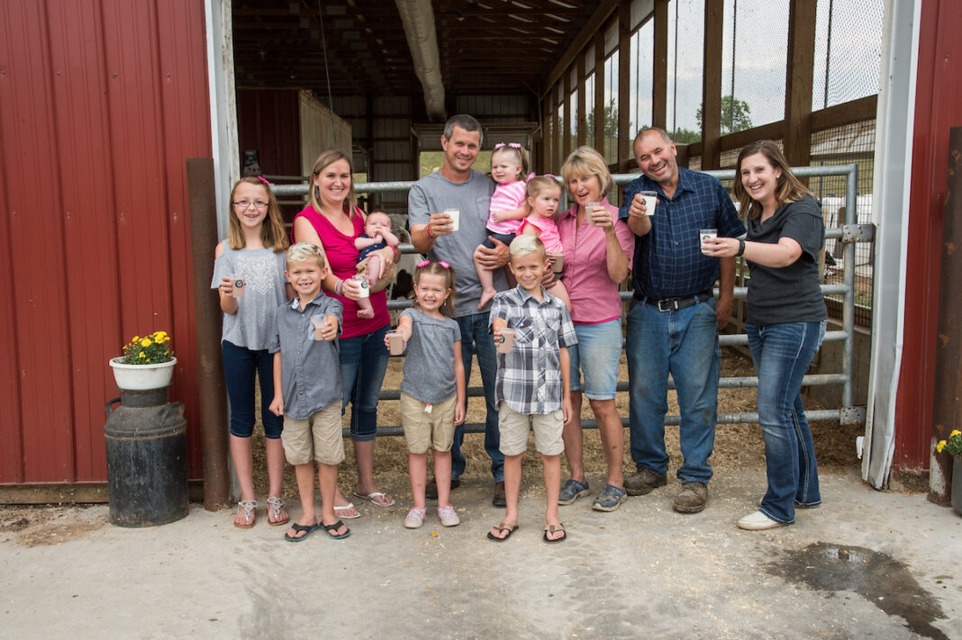 A group of people, including families and farmers, raising glasses of milk outside a barn at dairies in Michigan, celebrating local dairy farming and fresh milk production.