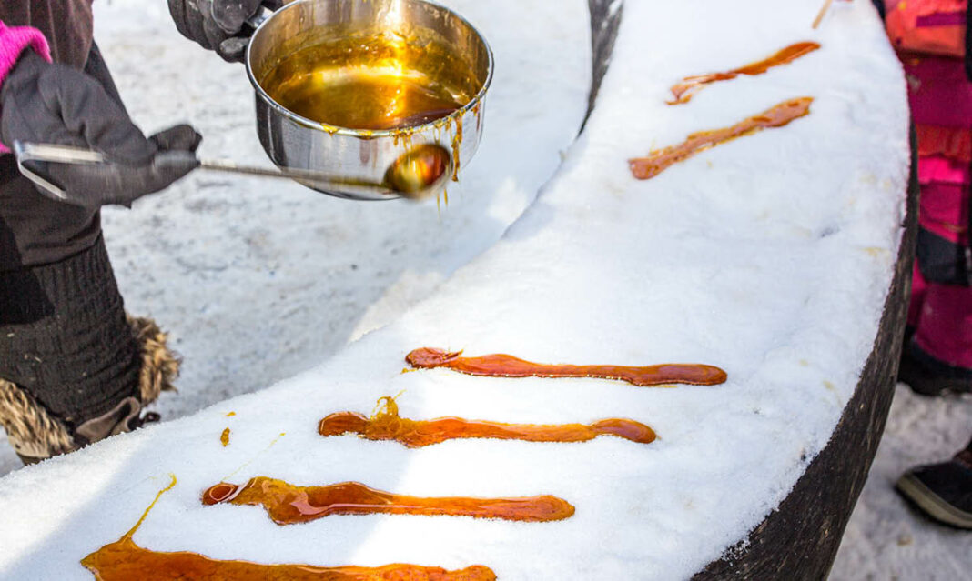 A close-up of maple taffy being poured onto fresh snow at a winter festival. The golden syrup hardens into a sweet treat, a traditional Canadian delicacy enjoyed during cold weather events.