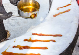 A close-up of maple taffy being poured onto fresh snow at a winter festival. The golden syrup hardens into a sweet treat, a traditional Canadian delicacy enjoyed during cold weather events.