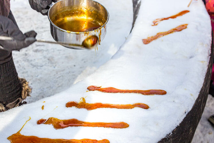 A close-up of maple taffy being poured onto fresh snow at a winter festival. The golden syrup hardens into a sweet treat, a traditional Canadian delicacy enjoyed during cold weather events.