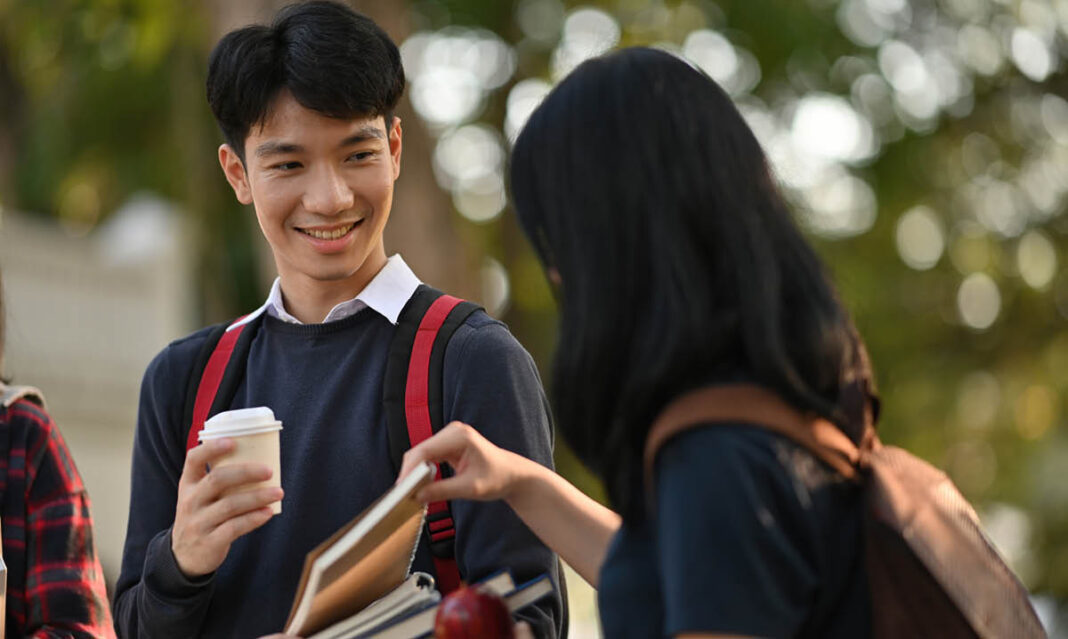 A female student borrows a book from a male friend while walking together