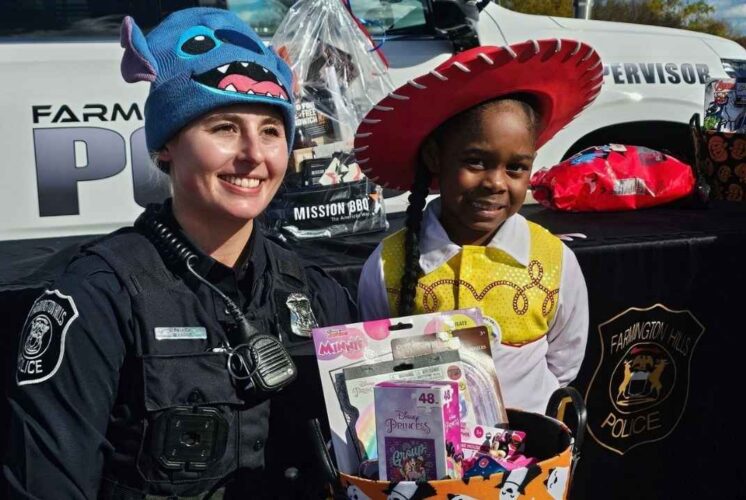 Farmington Hills Police officer and child in costume at trunk or treat Halloween event with candy and police car in