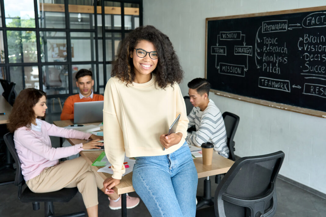 Confident high school student smiling while working on a group project with diverse classmates in a modern classroom setting focused on teamwork and strategic planning.
