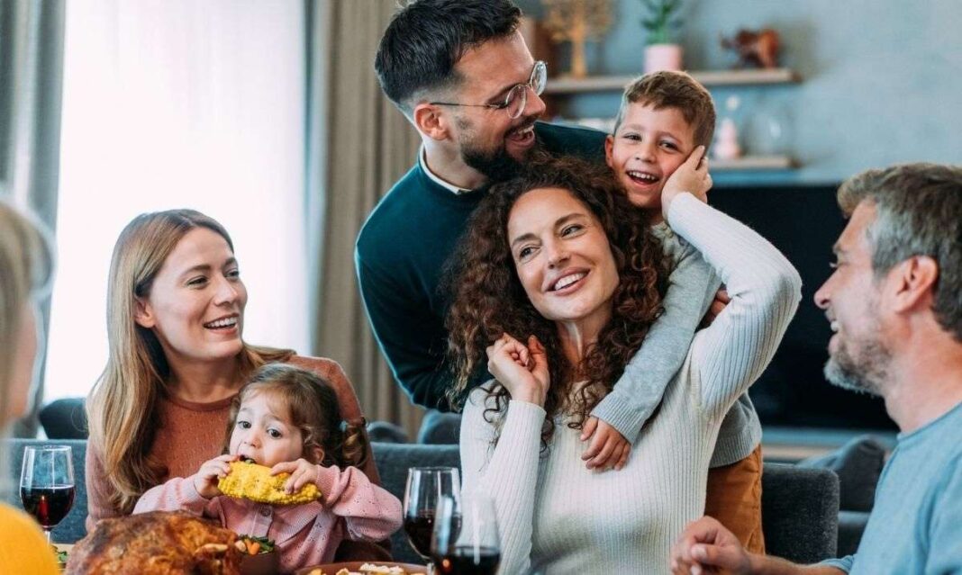 Parents and young children gathered around a Thanksgiving table with vegetables and healthy dishes, smiling and enjoying a relaxed family meal