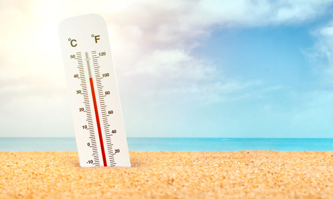 Thermometer in the sand near the ocean showing high temps