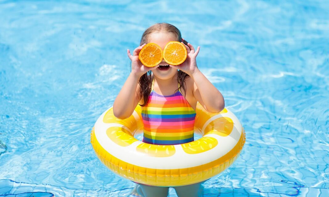 A little girl is playful in a swimming pool with a floaty that looks like an orange